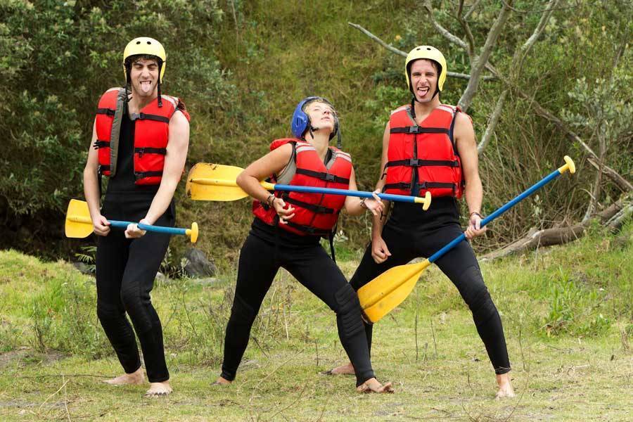 three people holding paddles and wearing lifejackets being funny