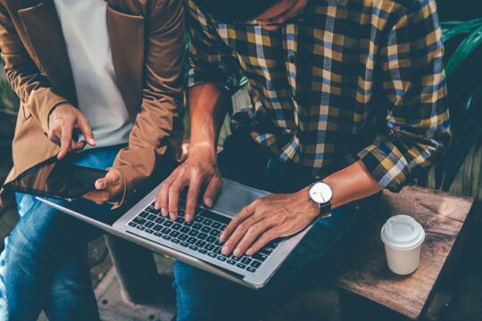 Couple sitting on a bench using a laptop