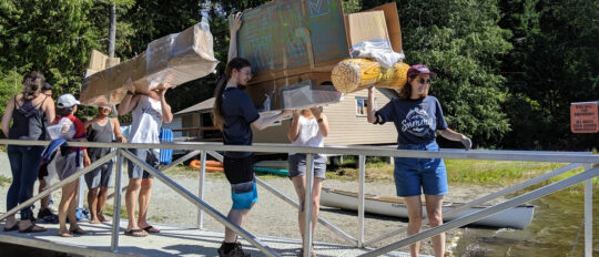 Checkfront employees carrying a homemade cardboard raft towards the water
