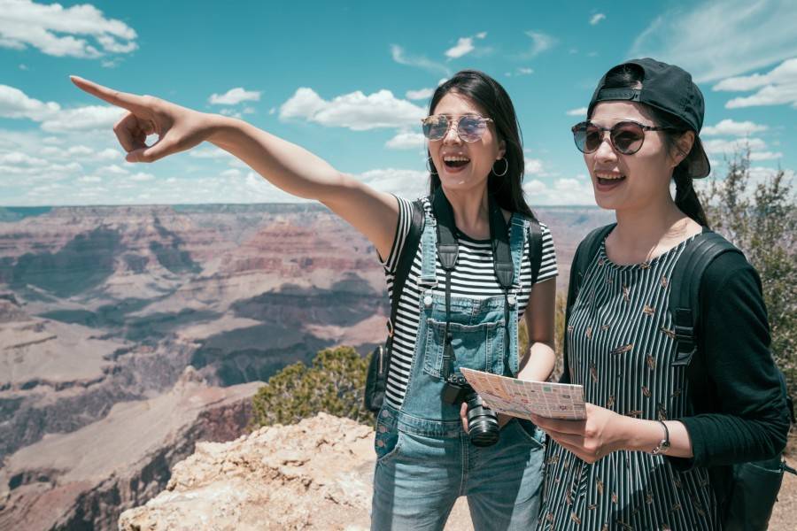 Two female chinese travelers pointing out at the view of the Grand Canyon.
