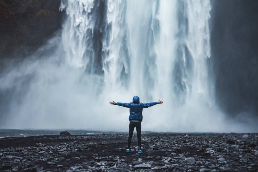 Traveler in blue jacket standing in front of waterfall in Iceland with arms wide
