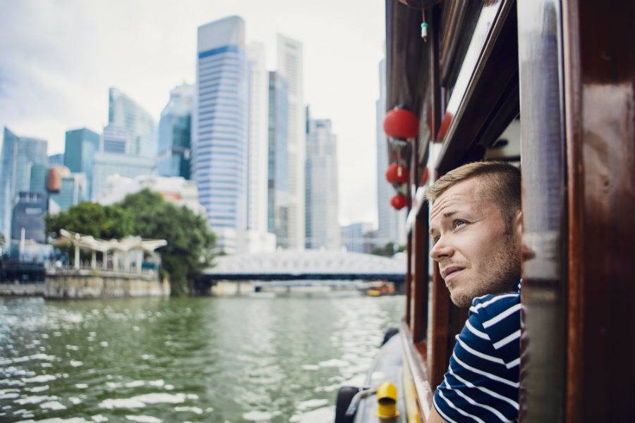 Young, male tour guide leading city boat tour in Asia looking out window at city landscape