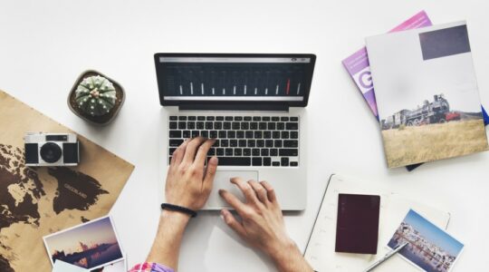 Hands resting on open laptop keyboard surrounded by travel items