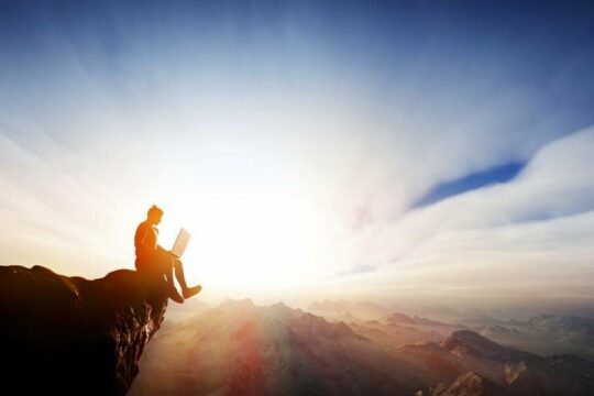 A person using a laptop on the edge of a cliff