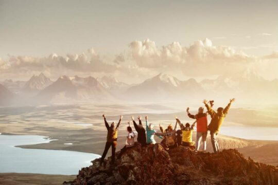 Group of people standing on mountain peak with arms in the air