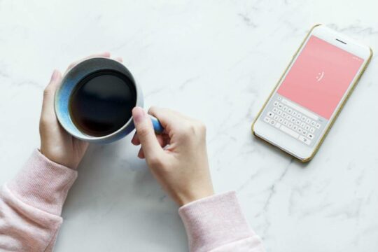 Close up of woman holding coffee cup with mobile device beside her