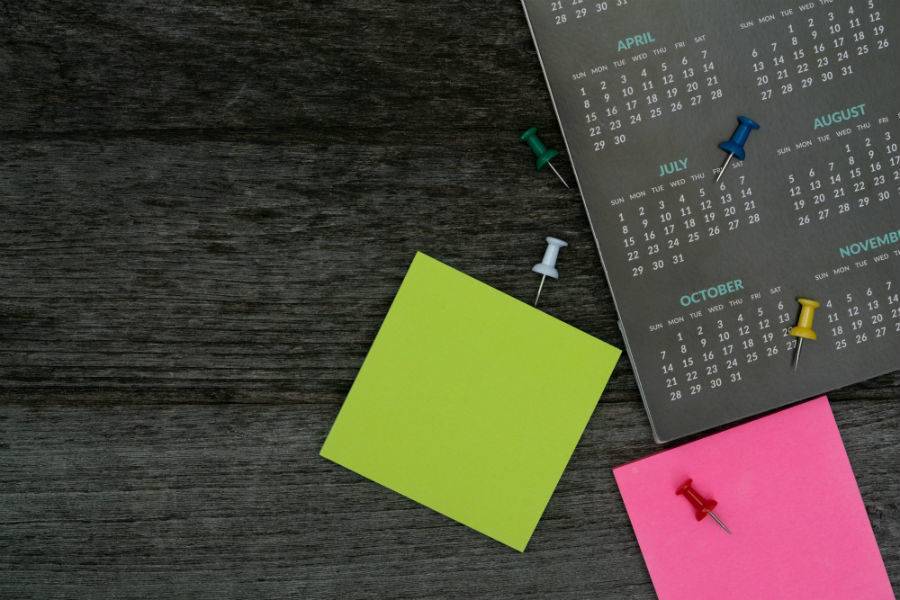 Sticky notes and thumb tacks scattered on a desk beside a calendar