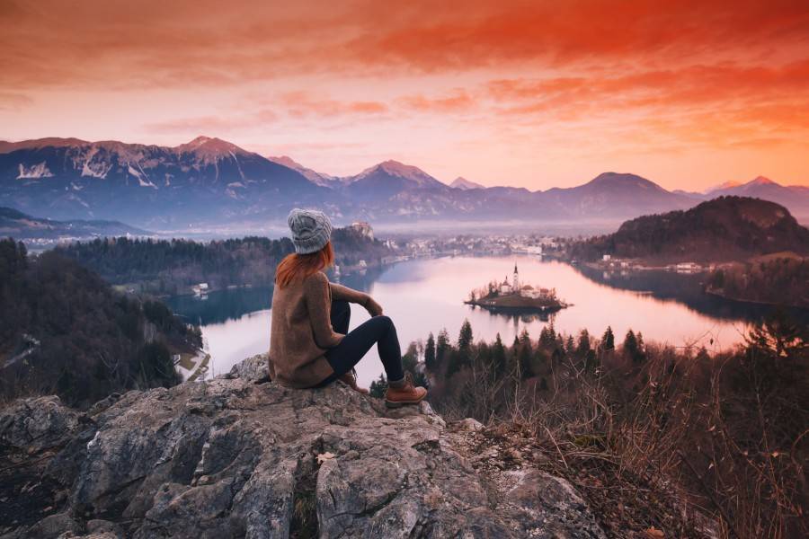 A woman sitting on a hill during a colourful sunset