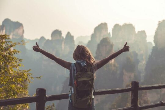 Woman on bridge with arms out facing the sunrise with thumbs up