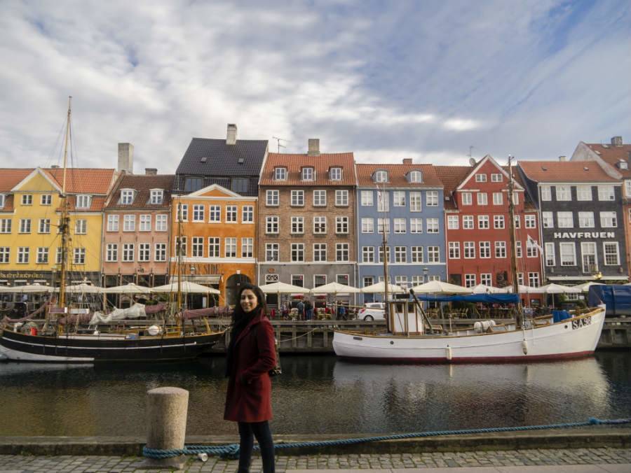 Woman standing beside water with boat and buildings in background