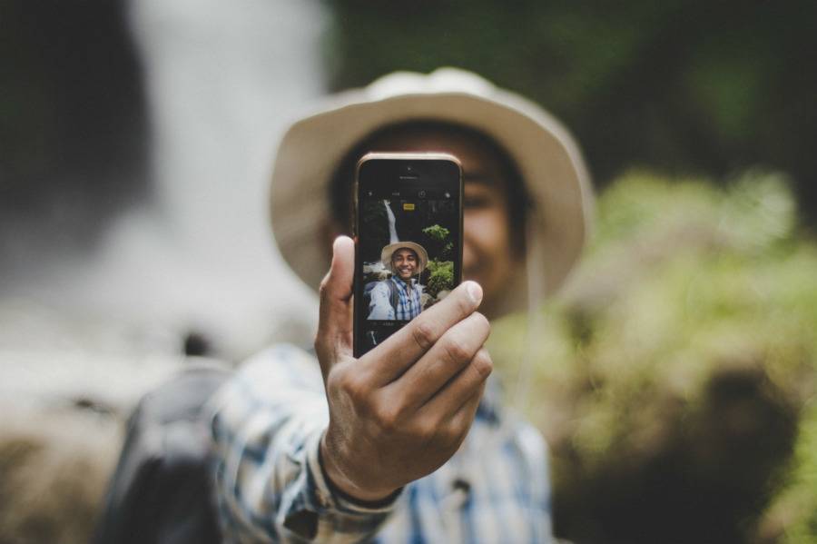 Traveler smiling taking selfie at tropical location with waterfall in the background