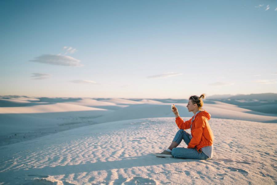 Female traveler booking on mobile at sand dunes wearing an orange jacket