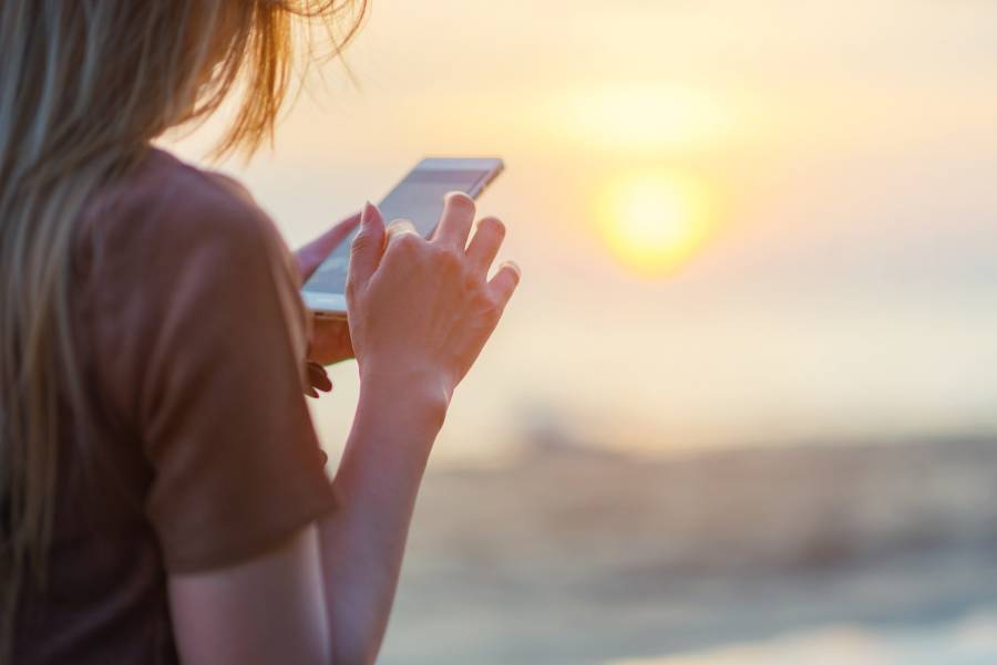 Traveler looking on mobile phone on the beach at sunset