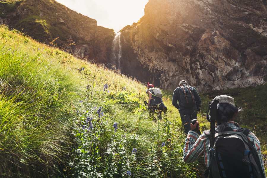 Group of hikers walking up hill toward waterfall in grassy field