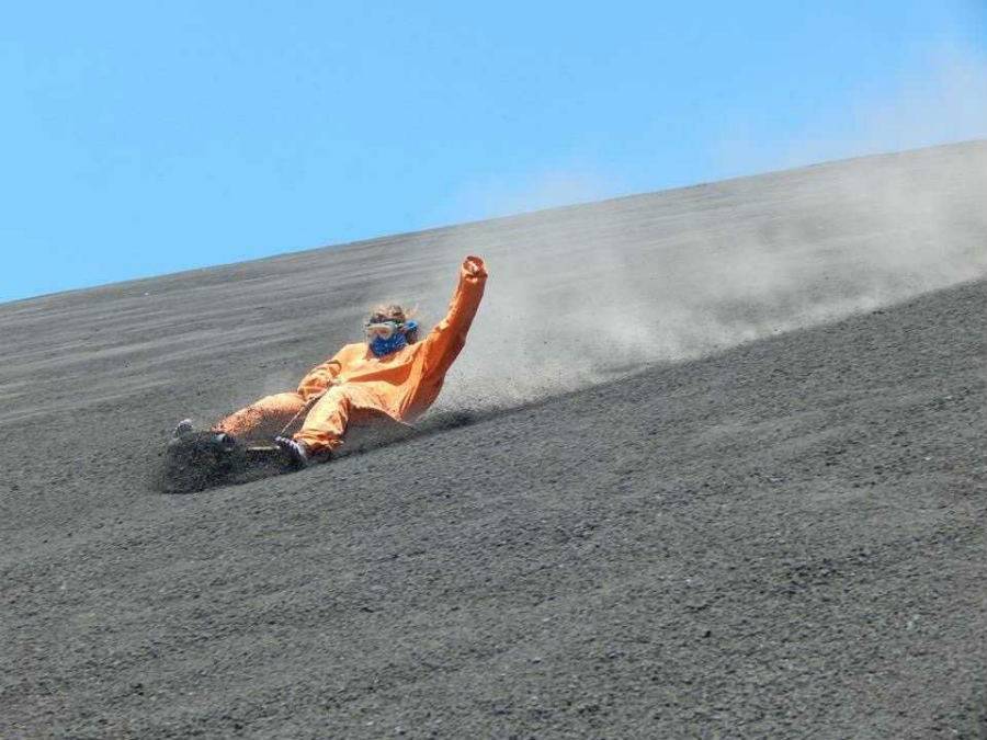 A solo traveler boarding down the side of an active volcano in orange jumpsuit