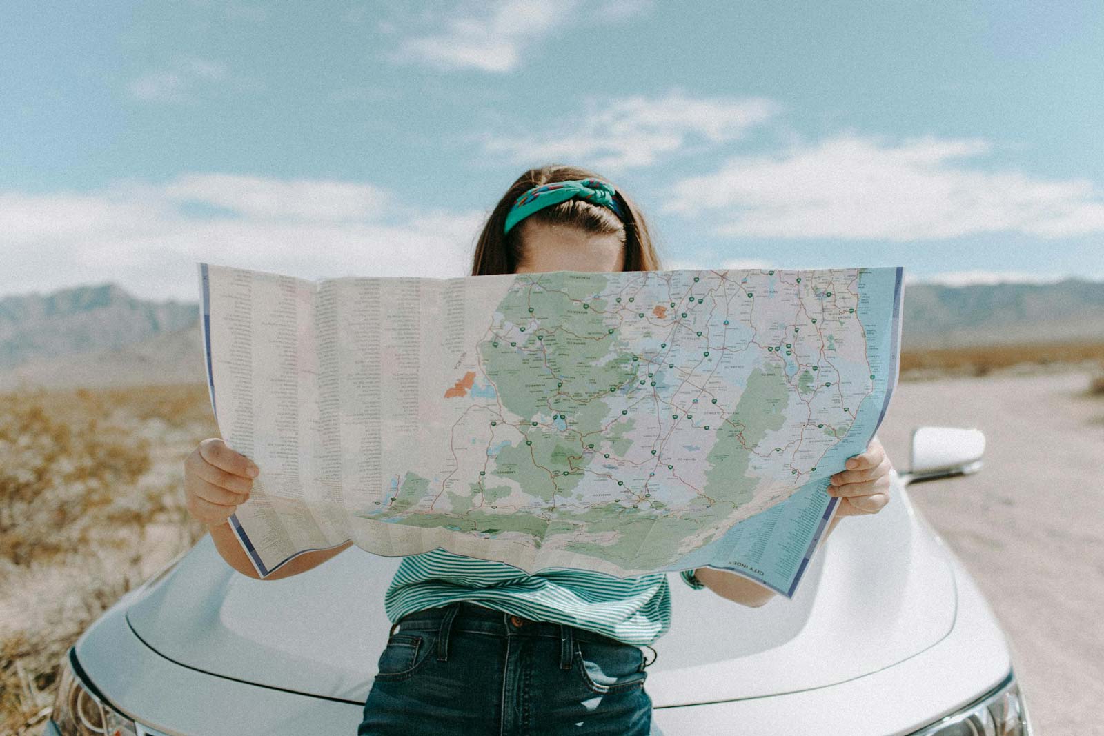 Woman Looking At The Map while sitting on a car's hood