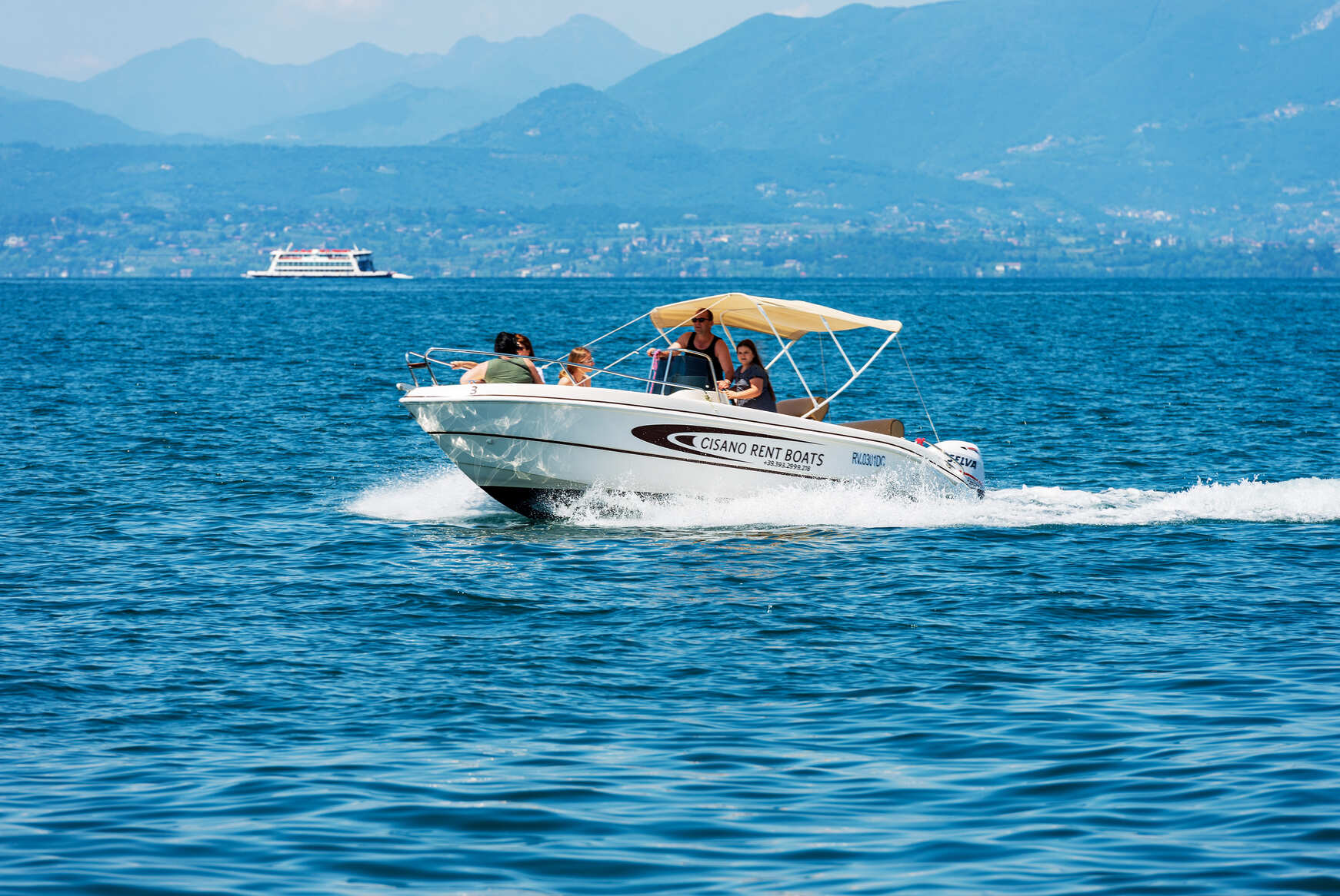 Group enjoying a boat rental from Cisano Rent Boats on a scenic lake, with mountains in the background, showcasing a leisure boating experience.