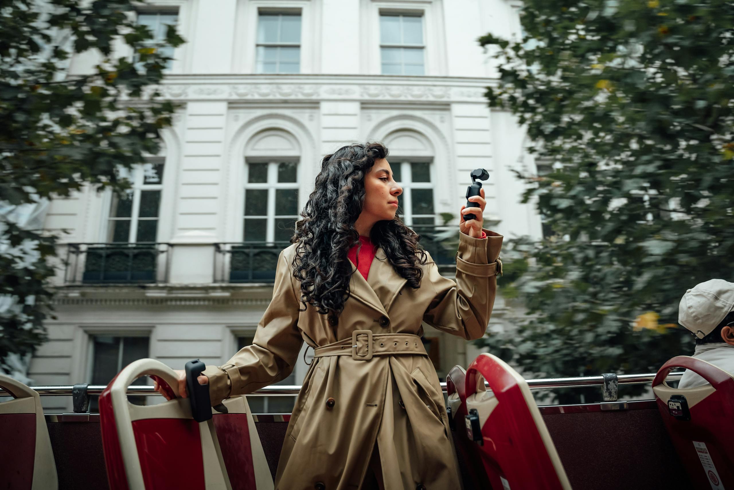 Woman filming with camera on open-top bus in London, capturing urban scenery. Elegant and cinematic shot.